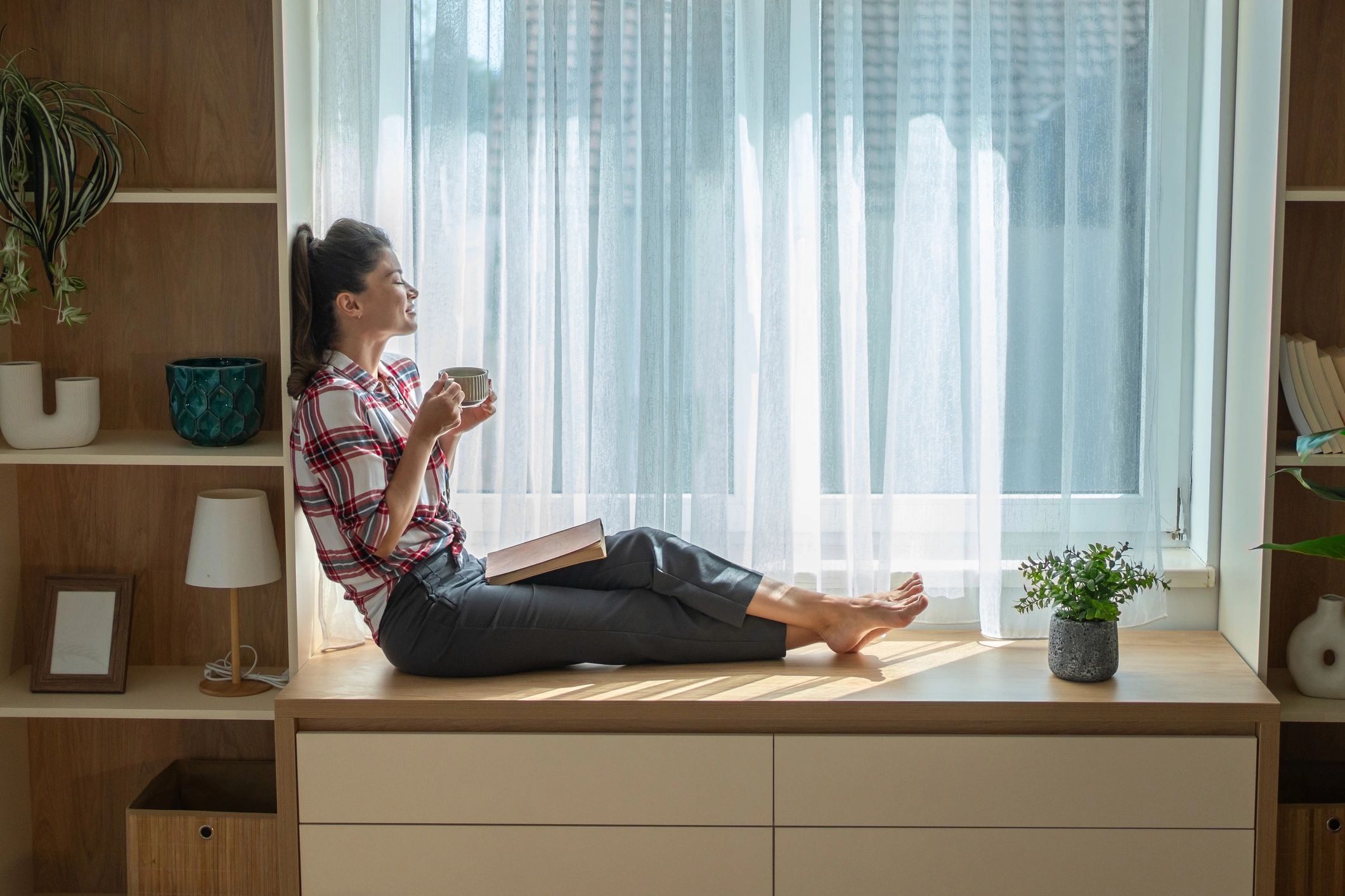 Reader by a sunlit window with a book and coffee